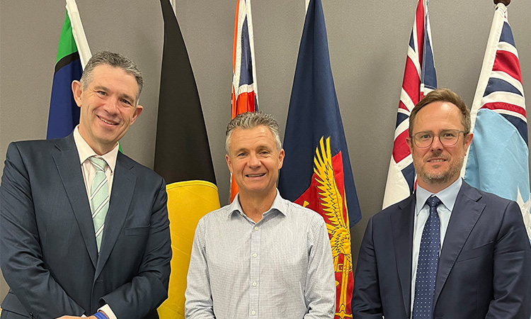 From left to right Simon Santow, Hon Matt Thistlethwaite MP and Damian Ogden standing in front of a row of flags